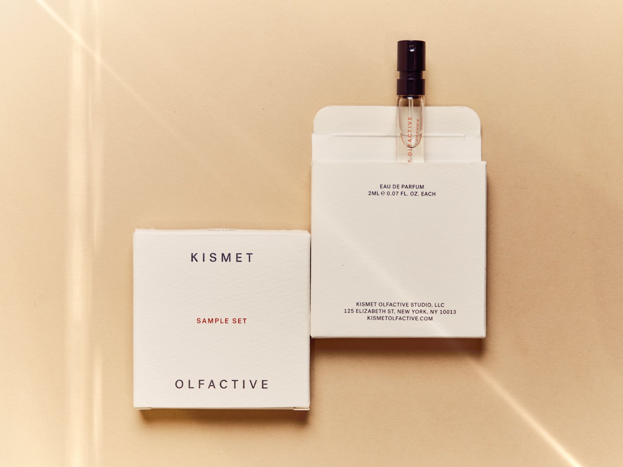 white kismet olfactive sample set box on a beige background and one perfume sample vial peeking out of box