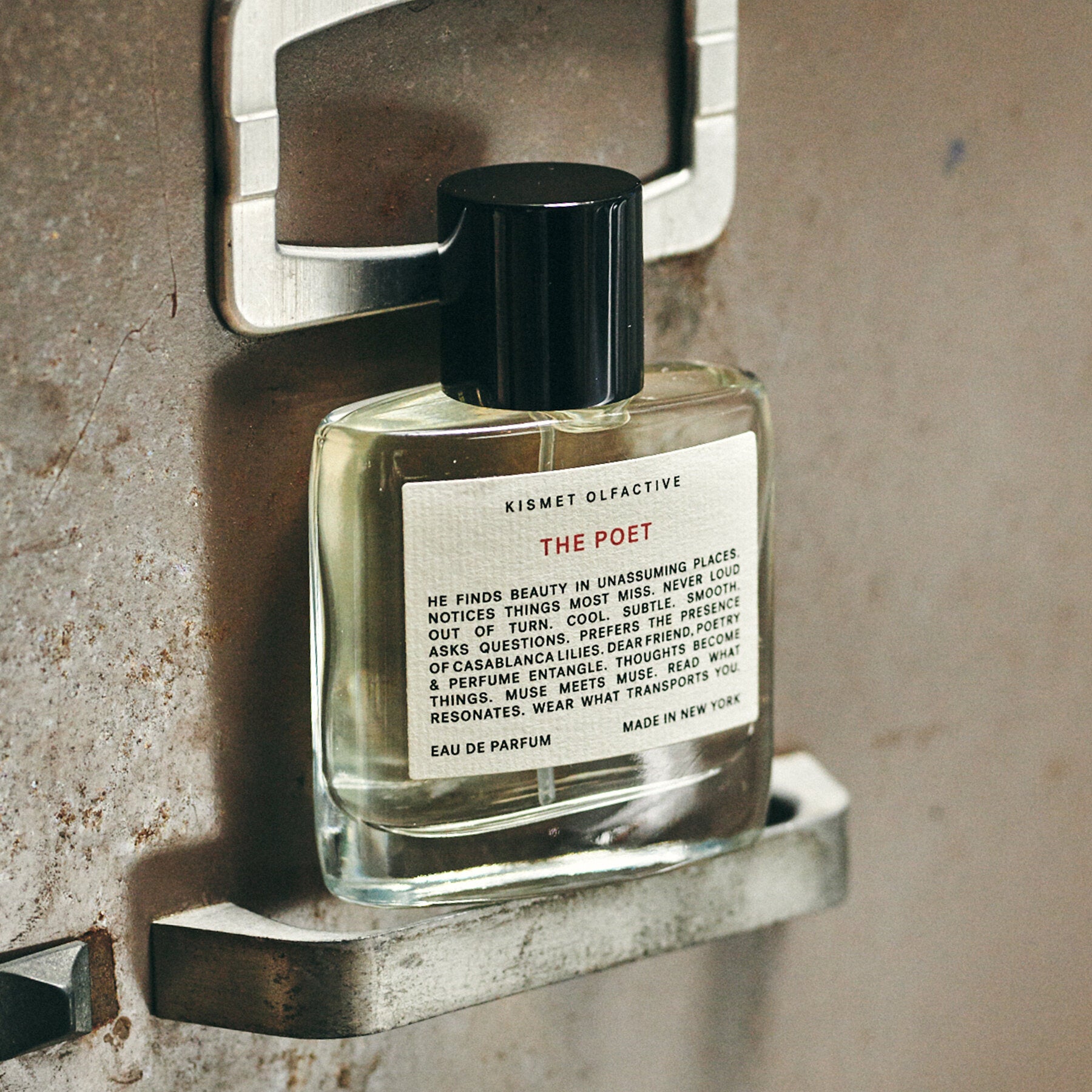 perfume bottle with black cap and label that says "the poet" against a concrete background