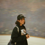 Person wearing a black cap and dark clothing in front of a large abstract painting.