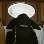 Black plush hat with 'FEELINGS' text on a wooden cabinet.