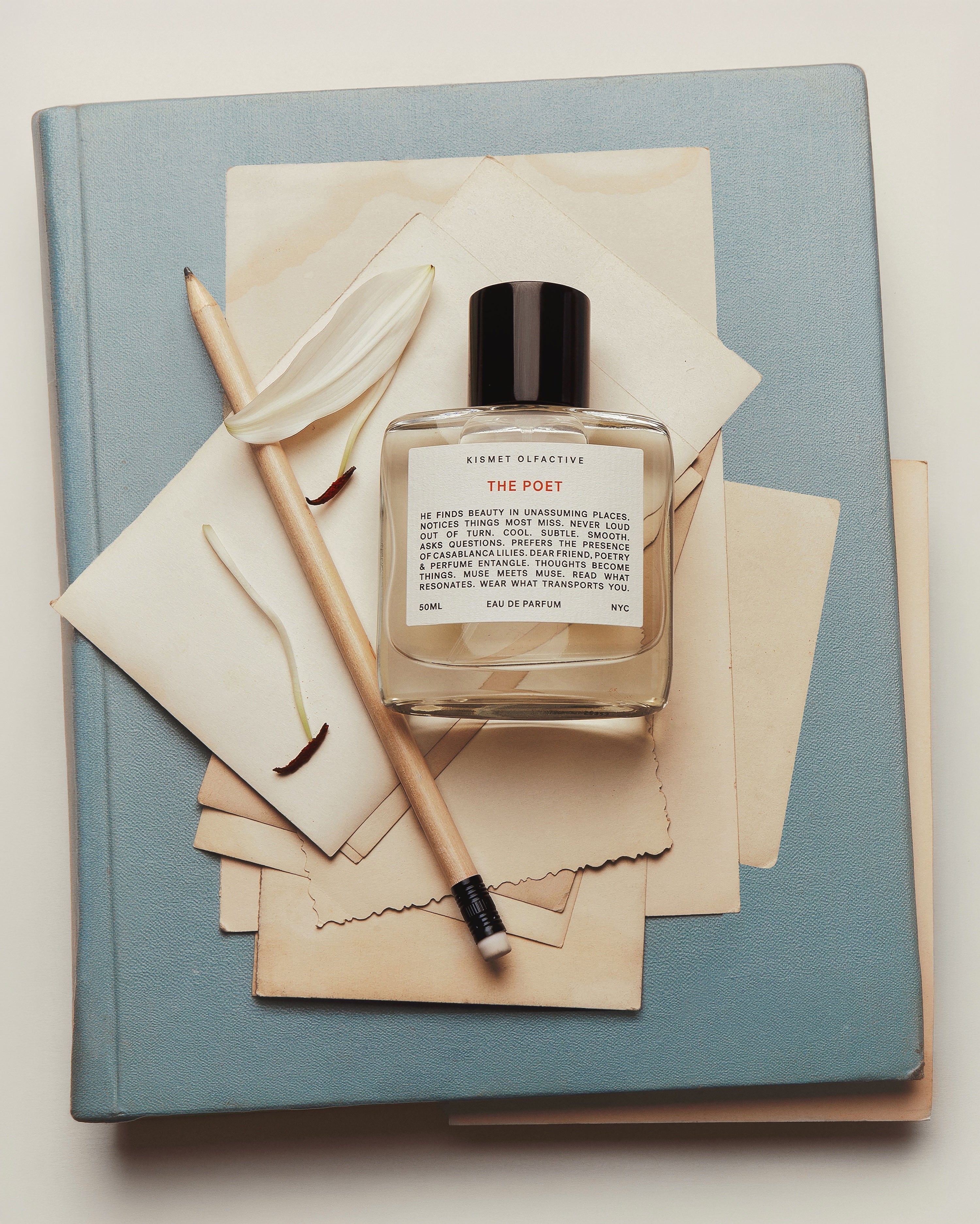 Perfume Bottle The Poet on top of a note book, envelope, papers, and a pen. 