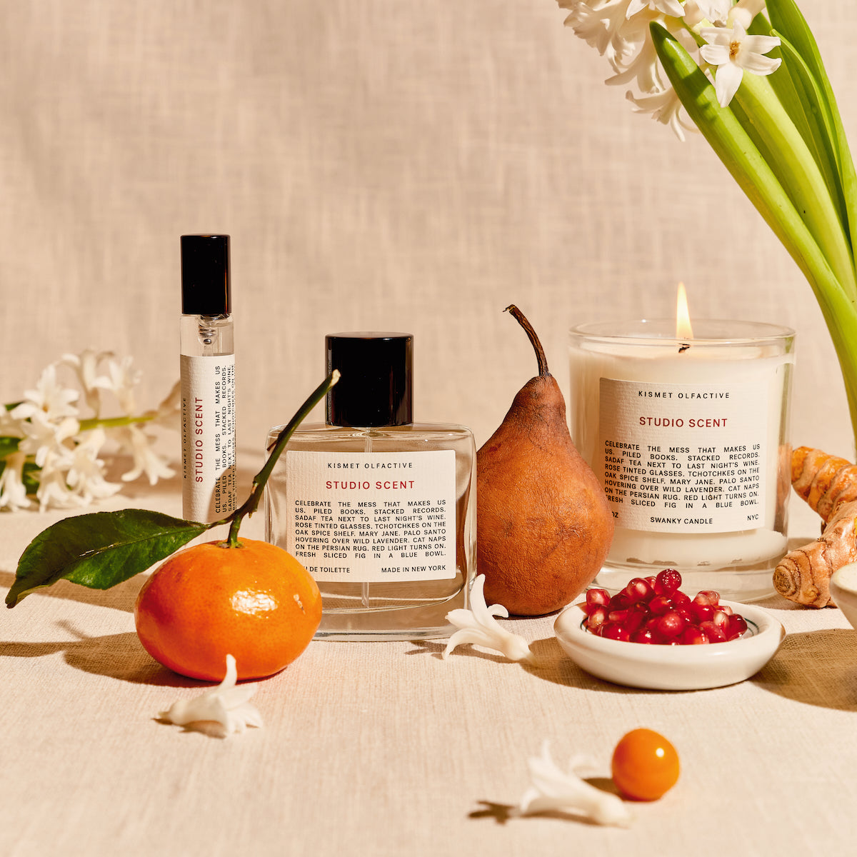 Studio Scent products including a candle, perfume, and flowers on a pink background