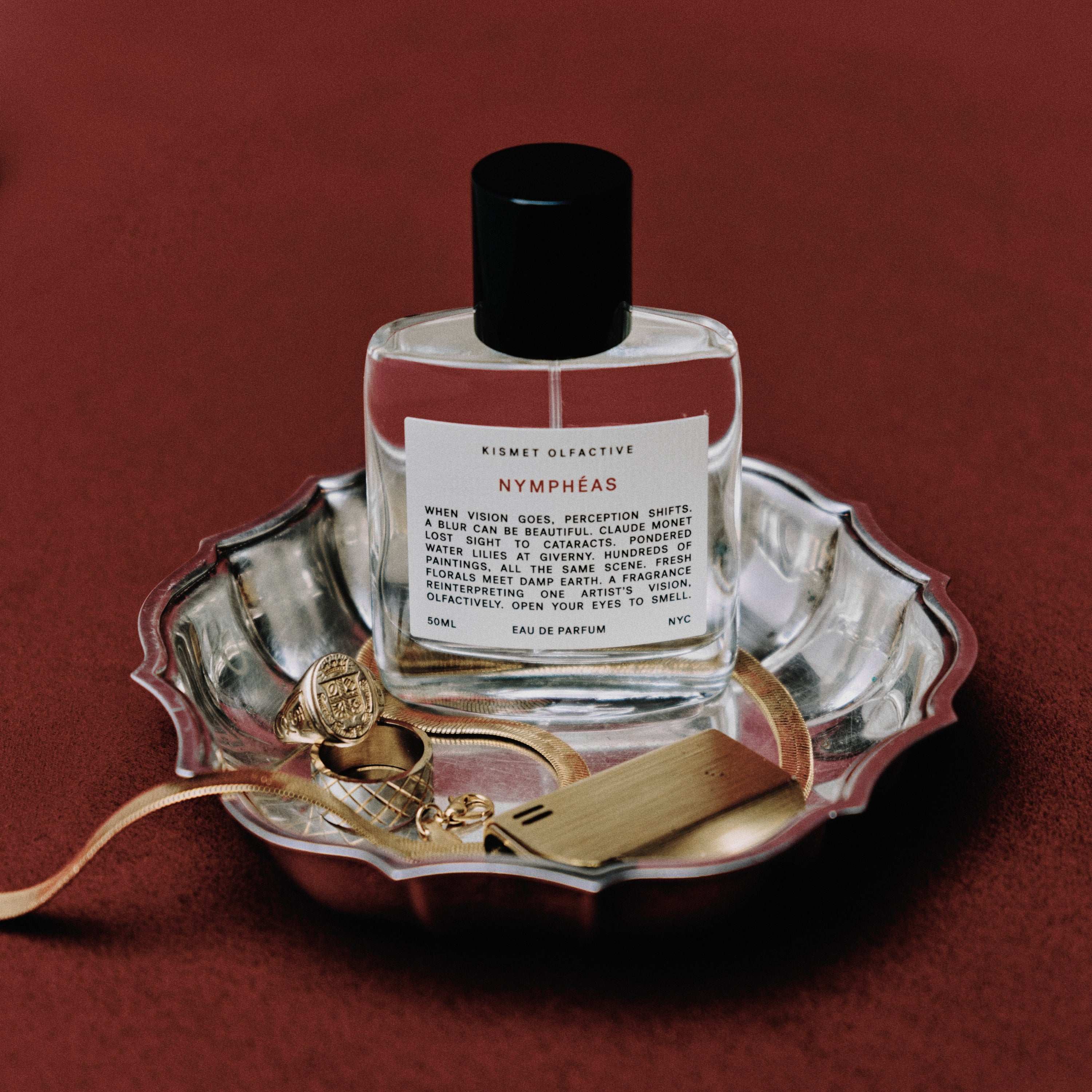 Perfume bottle labeled 'Nymphaéas' on a decorative tray with gold accents against a red background
