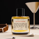 Vetiver Supreme 50ml bottle on a table with a leather item and a martini glass. 