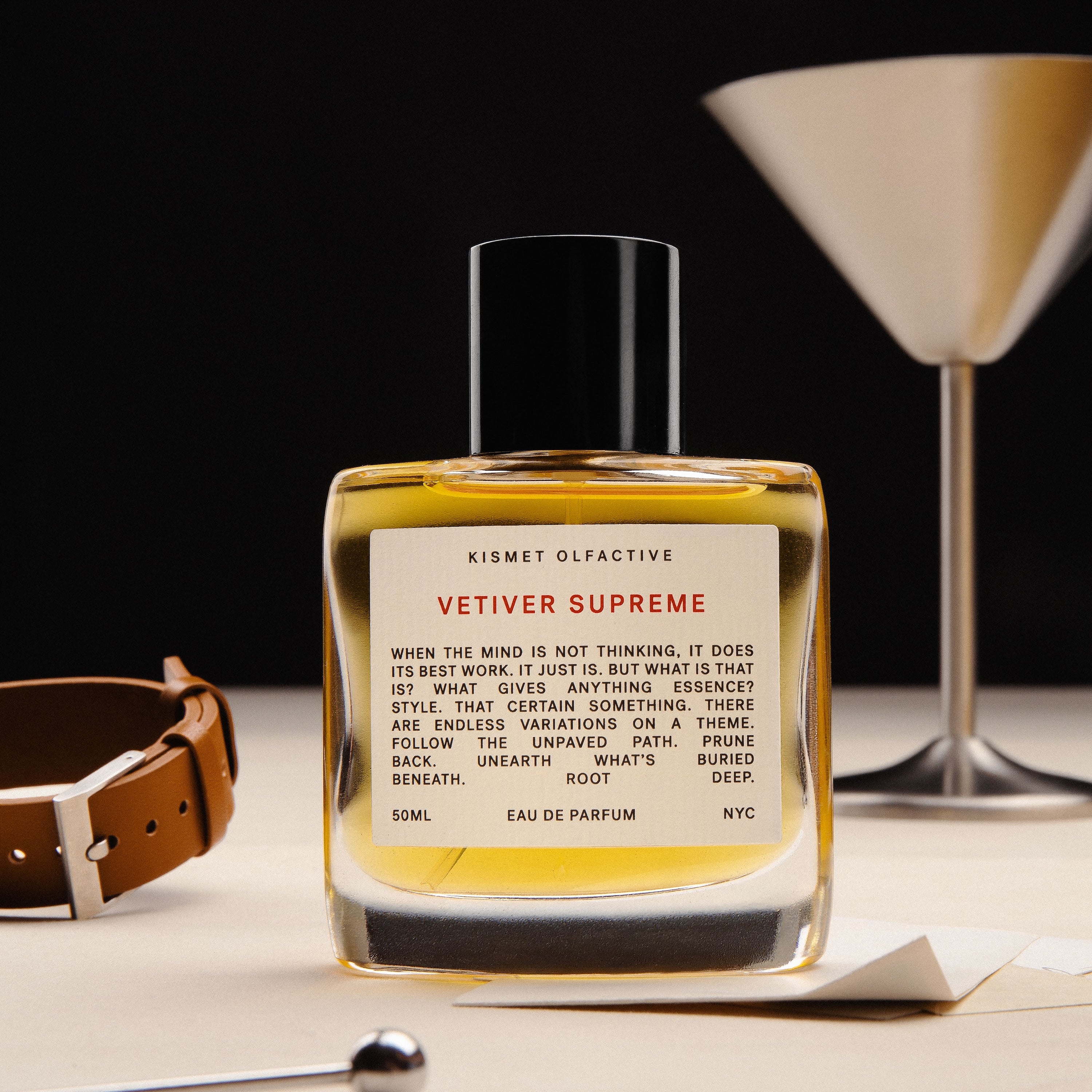 Vetiver Supreme 50ml bottle on a table with a leather item and a martini glass. 