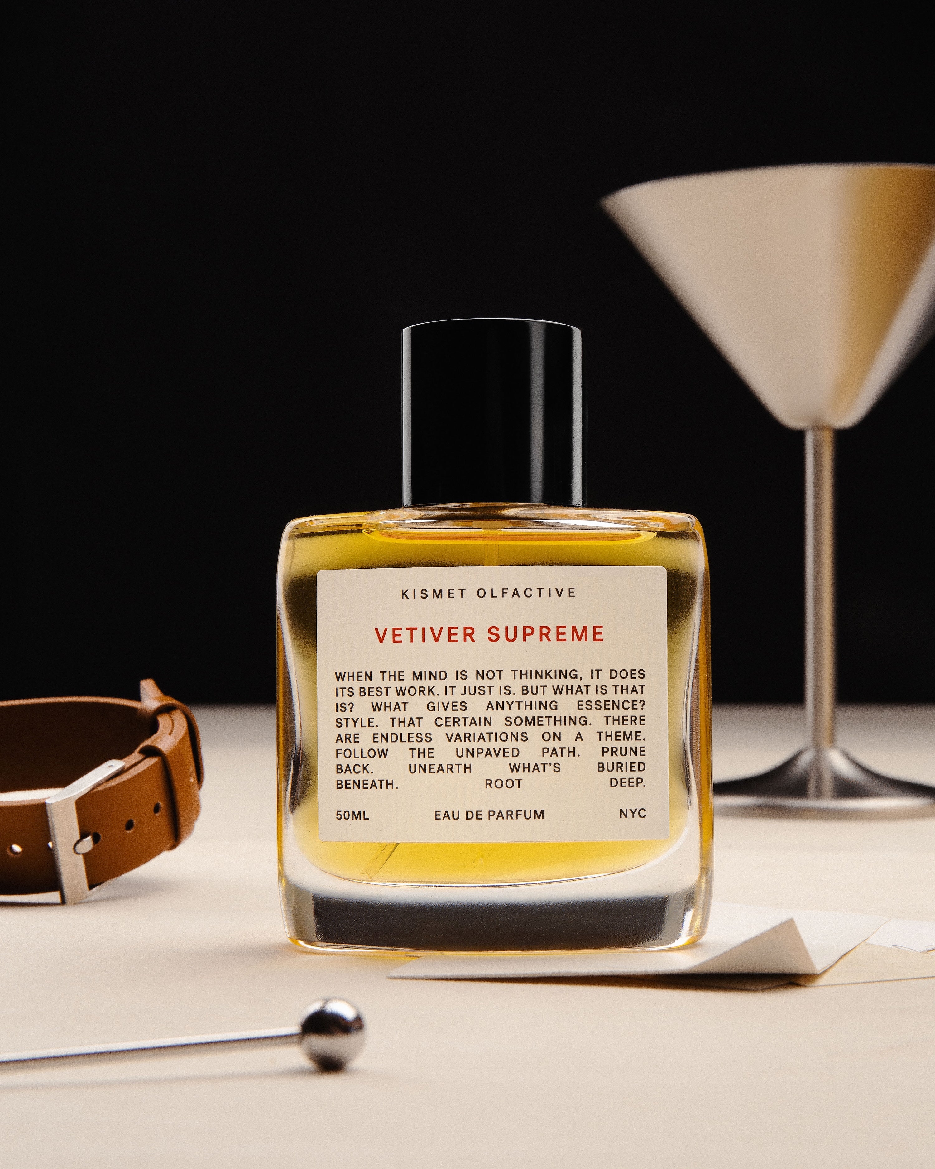 Vetiver Supreme 50ml bottle on a table with a leather item and a martini glass. 